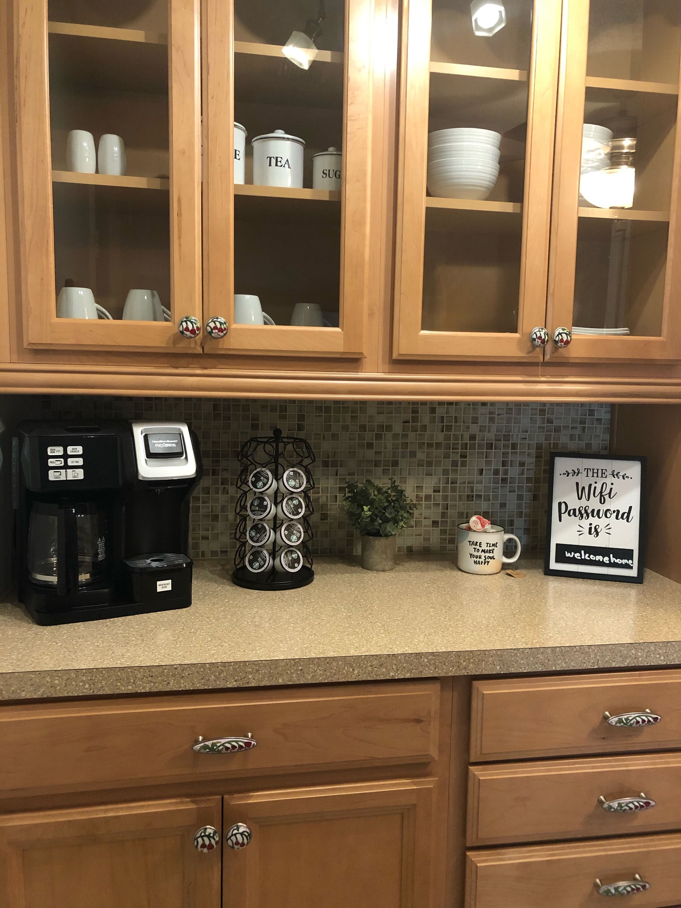 Une cuisine avec des placards en bois, une machine à café, une tasse et un panneau indiquant le mot de passe du Wi-Fi.