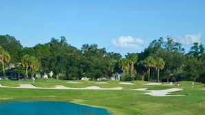 Un parcours de golf avec des bunkers de sable, un étang et des arbres denses en arrière-plan.