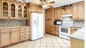 Une cuisine avec des meubles de rangement en bois, un réfrigérateur, un four et un ventilateur de plafond.