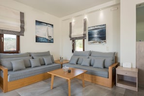 A modern living room with two grey sofas, a wooden coffee table, and a small wooden nightstand.