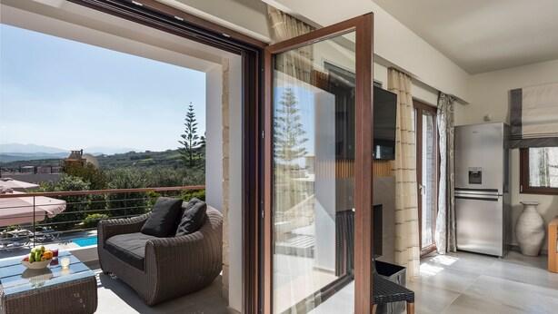 Een balkon met rieten meubilair, een glazen deur en uitzicht op een zwembad en bergen.