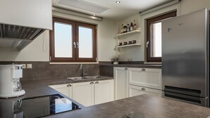 Een moderne keuken met witte kasten, een roestvrijstalen koelkast, een koffiezetapparaat en een raam met bruine kozijnen.