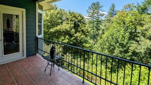 Un balcon doté d’une balustrade en métal, d’une chaise et offrant une vue sur une zone boisée.