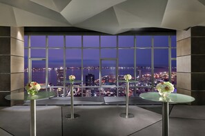 A modern interior with a panoramic city view, two glass tables with floral centerpieces, and a geometric ceiling design. - Intercontinental Luanda Miramar by IHG (Luanda)