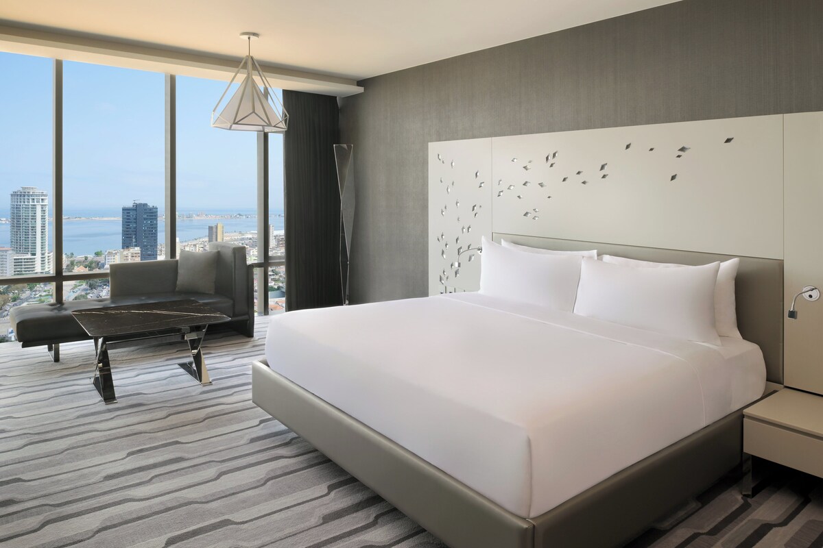 Een moderne hotelkamer met een groot bed, een bank, een bijzettafeltje en uitzicht over de stad.