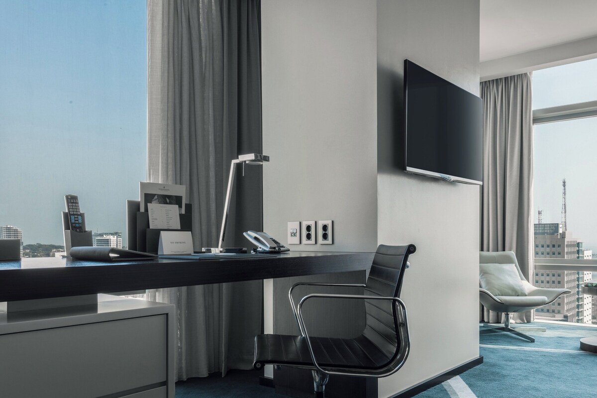 Een moderne hotelkamer met een bureau, stoel en een grote televisie aan de muur.