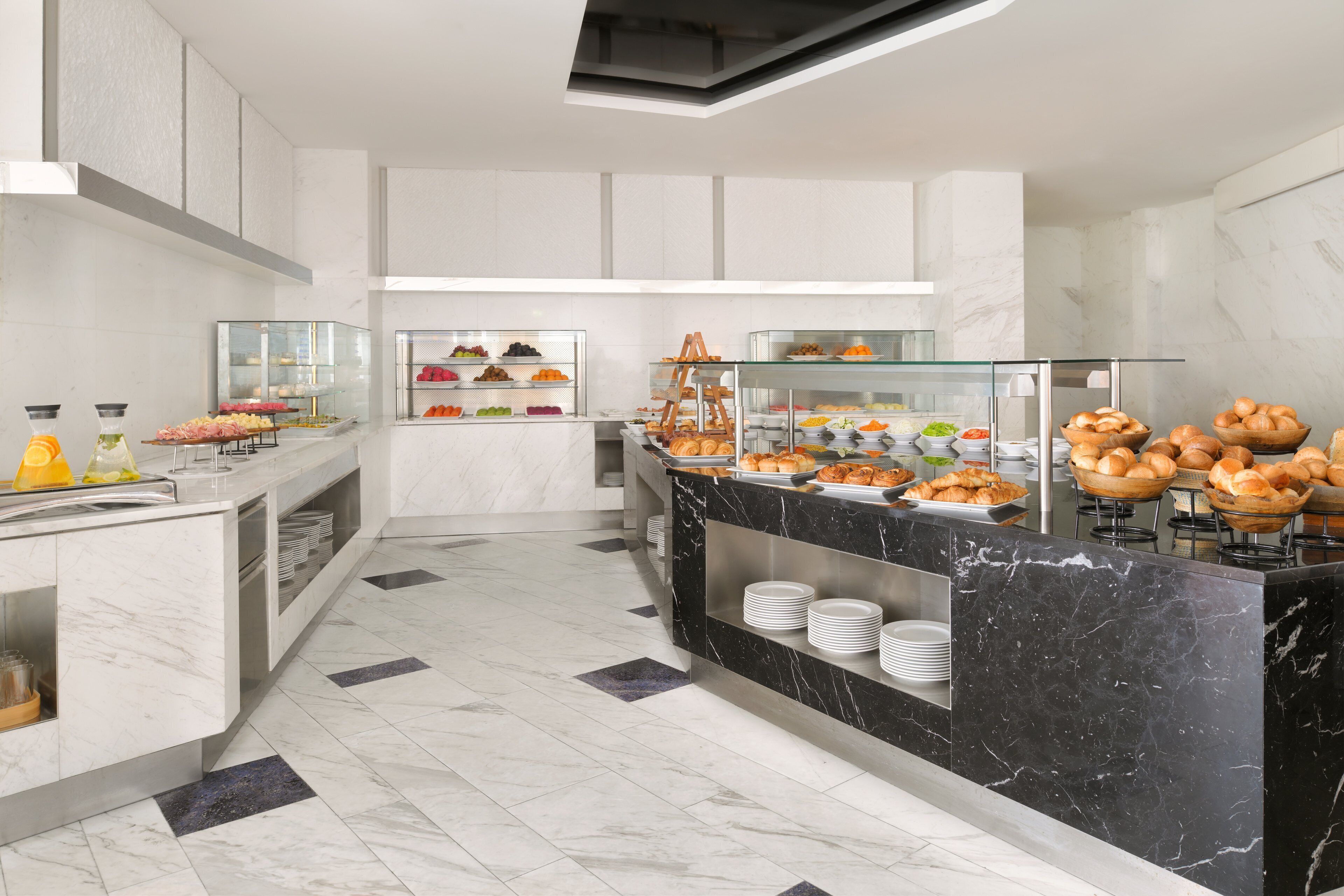 A modern hotel kitchen with marble countertops, glass display cases, and a variety of food items.