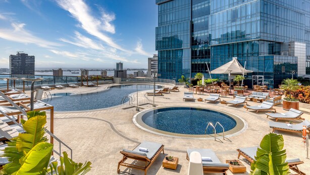 A rooftop pool area with lounge chairs and a large glass building in the background. - Intercontinental Luanda Miramar by IHG (Luanda)