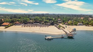 An aerial view of a beach resort with a pier, beach umbrellas, and a boat dock. - Intercontinental Luanda Miramar by IHG (Luanda)
