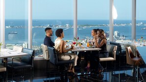 A dining area with a city view, large windows, and a table set with food and drinks. - Intercontinental Luanda Miramar by IHG (Luanda)