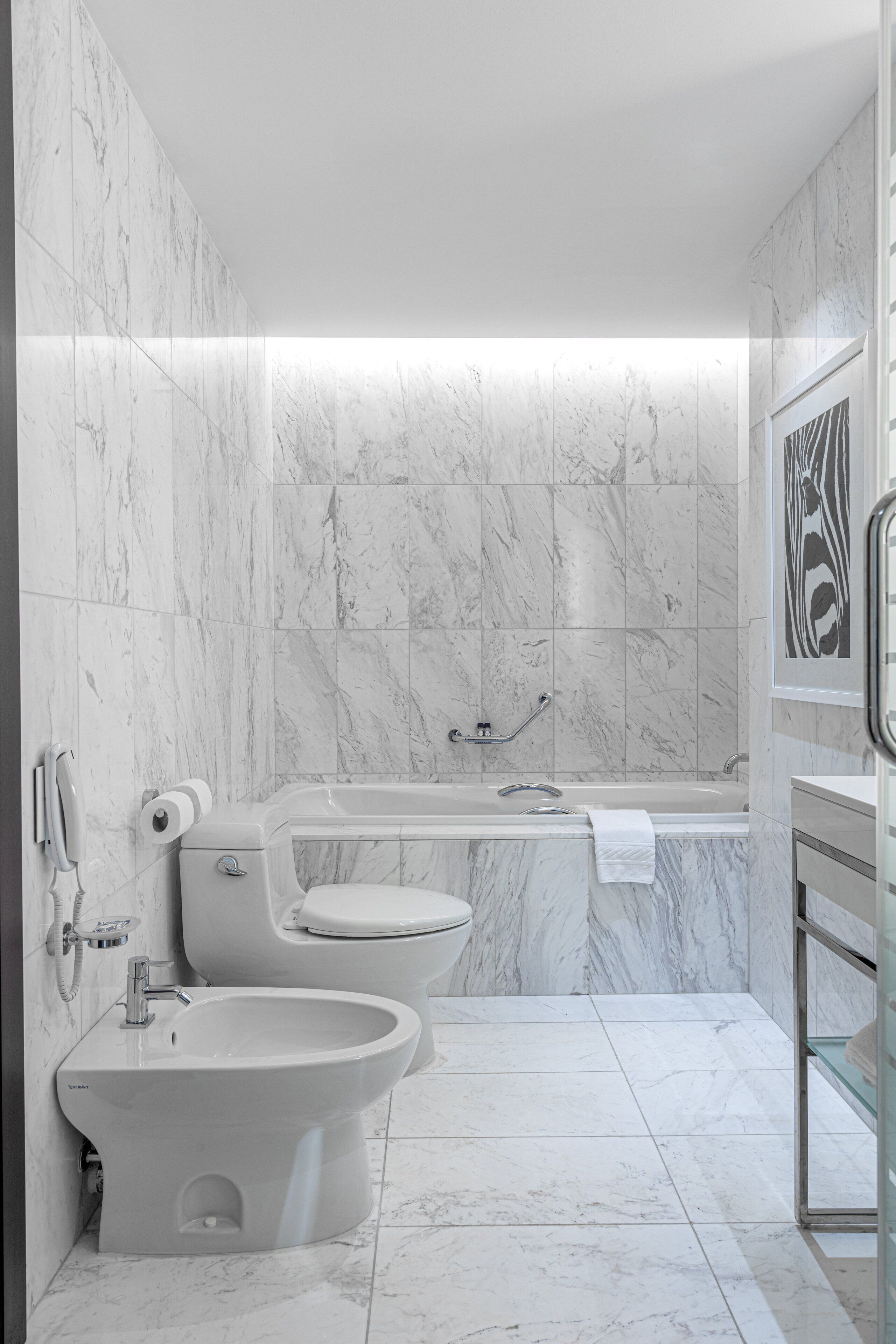 A modern bathroom with a bidet, toilet, and bathtub, all with marble walls and floors.