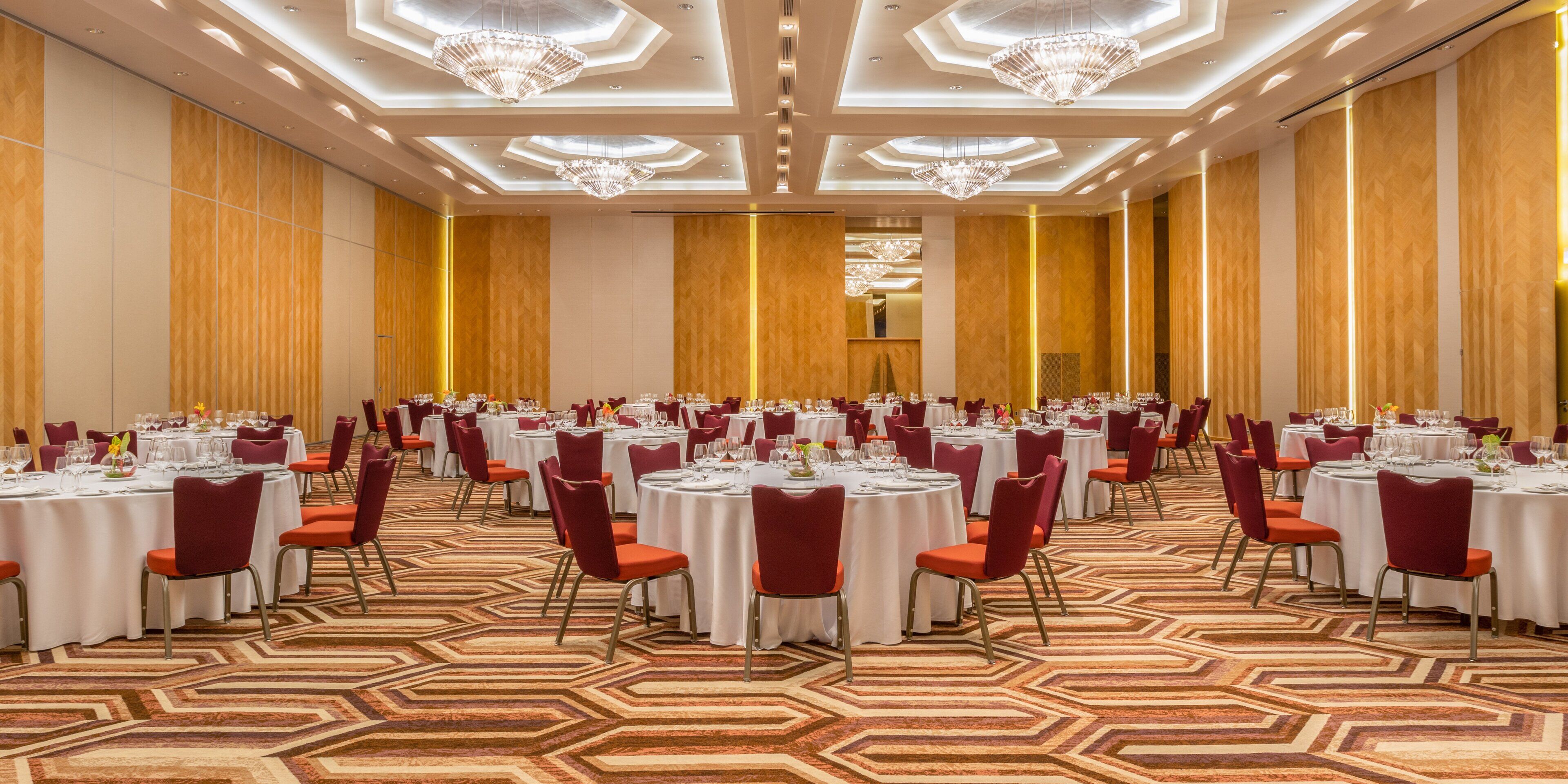 Une salle de banquet avec des tables rondes, des chaises rouges et des lustres.