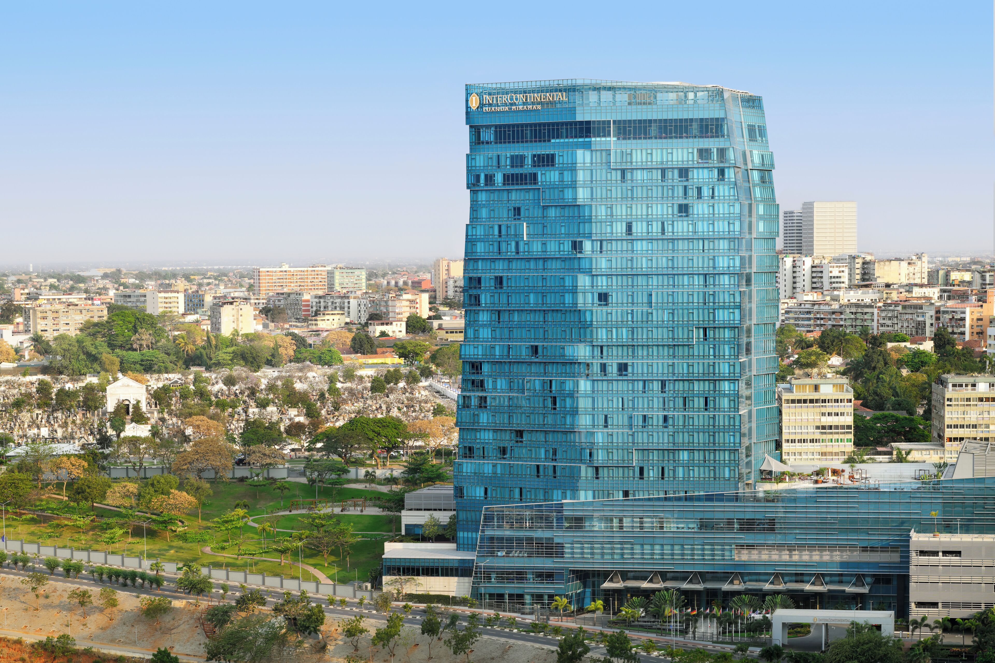 Un moderno edificio de gran altura con fachada de vidrio, rodeado de un paisaje urbano y vegetación.