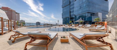 A rooftop pool area with sun loungers and a central pool, surrounded by modern buildings.