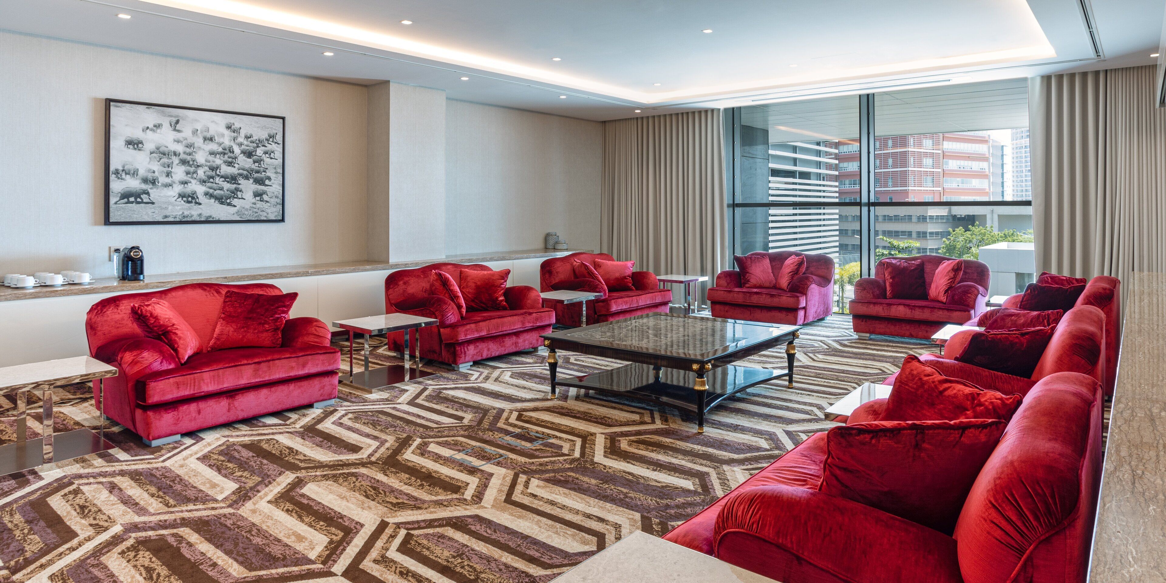 Un salon moderne avec des canapés en velours rouge, une table basse en verre et un tapis à motifs.
