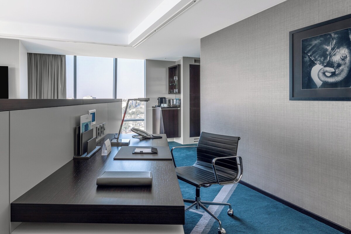 Een hotelkamer met een bureau, stoel en een groot ingelijst schilderij aan de muur.