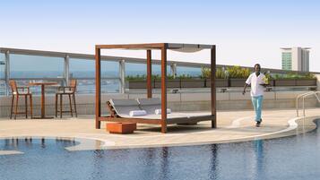 Relax by the pool with a clear view of the city skyline, surrounded by a glass railing and comfortable lounge seating.
