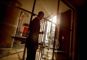 A man in a suit standing in front of a glass door with a reflection of a chandelier and a sign that reads "ERCONTINENTAL".