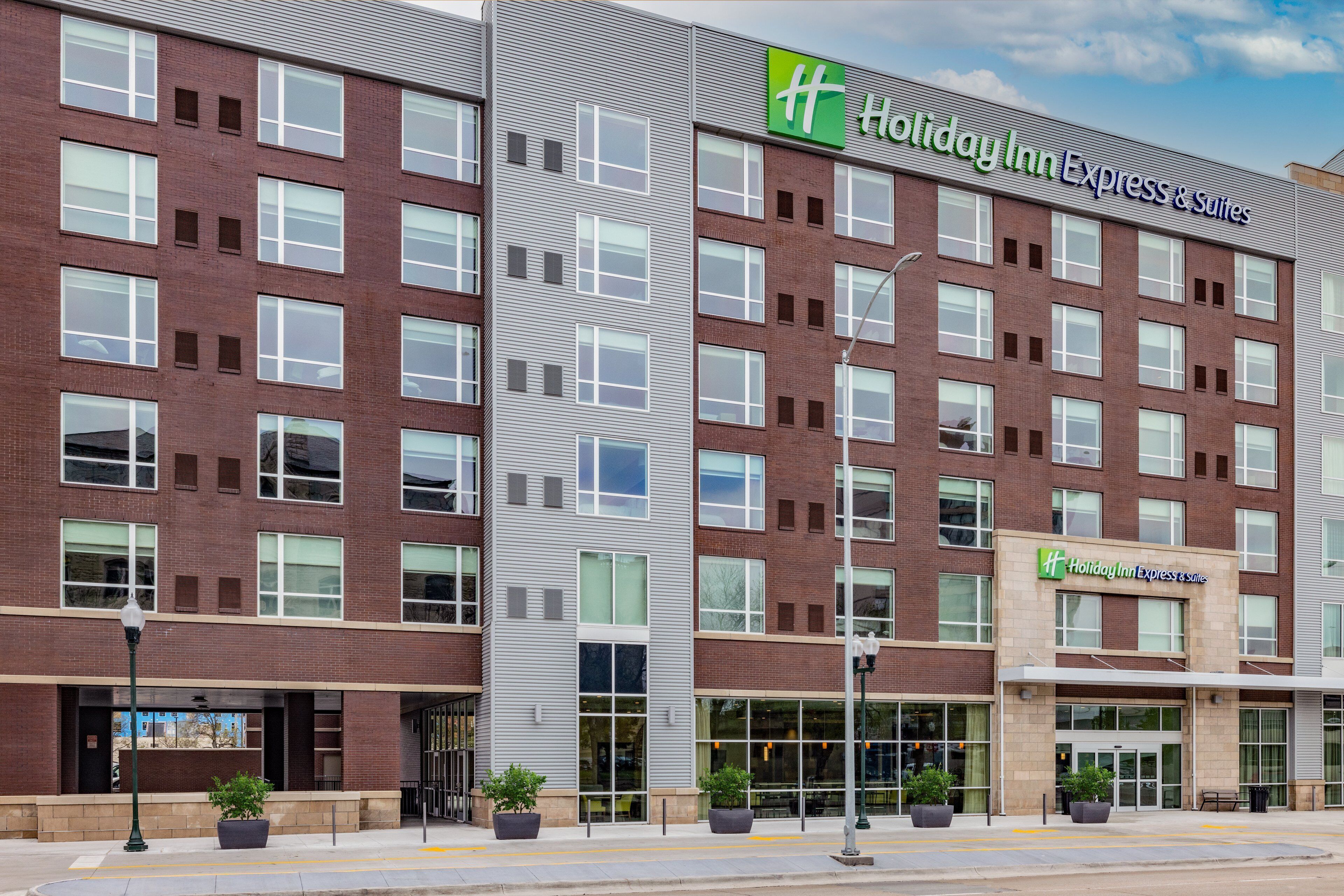 A Holiday Inn Express & Suites building with a brick facade, large windows, and potted plants at the entrance.