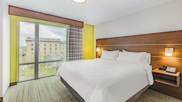 Une chambre d’hôtel avec un grand lit, une table de chevet avec un téléphone, une fenêtre donnant sur des immeubles et un luminaire au plafond.