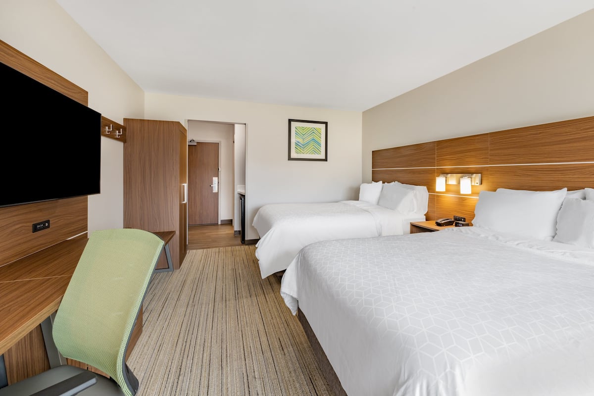 A hotel room with two beds, a TV, a desk, and a wooden headboard.