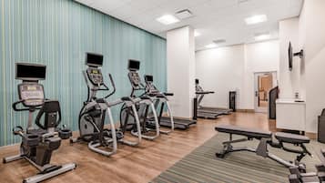 Un gimnasio con cintas de correr, elípticas y una banca.