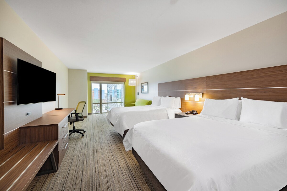 Habitación de hotel con dos camas, televisión de pantalla plana, escritorio y vista a la ciudad.
