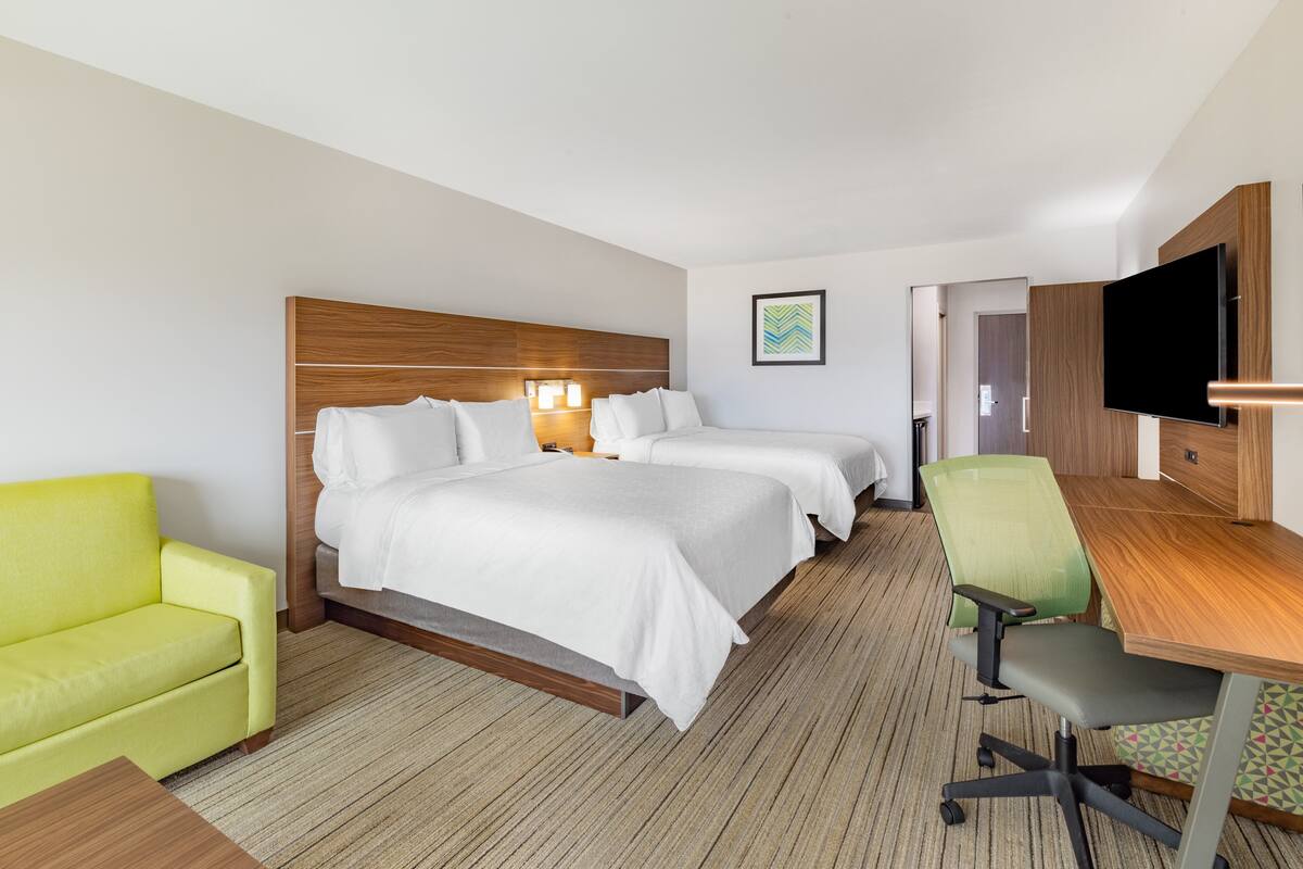A hotel room with two beds, a desk, a television, and a green armchair.
