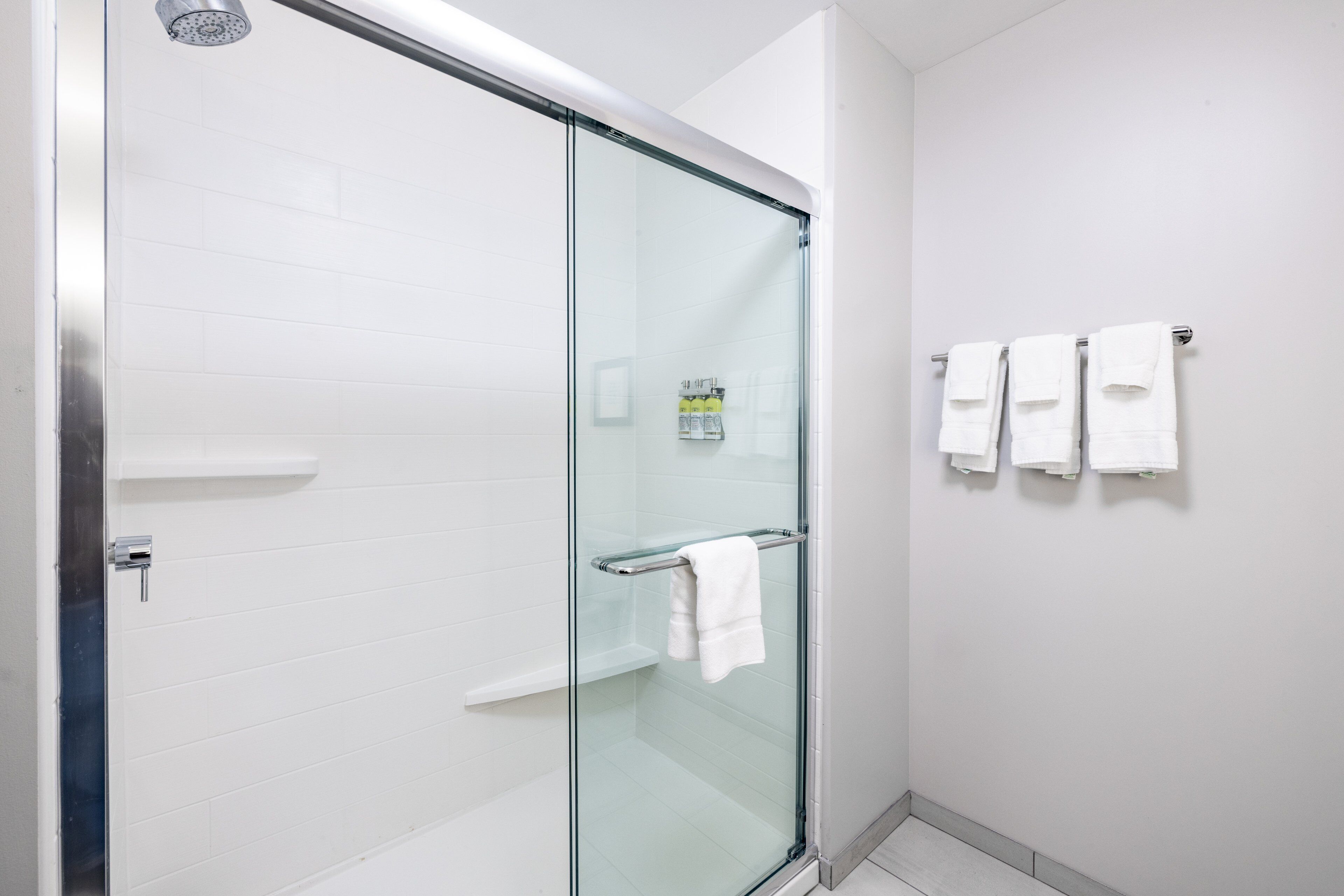 A modern bathroom with a glass shower enclosure, white tiled walls, and a towel rack with multiple towels.