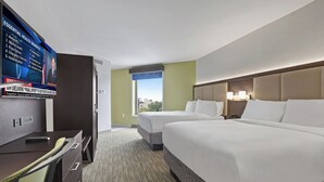 A hotel room with a large bed, a desk with a chair, a television displaying a news broadcast, and a window with a city view. - Hotel 1200 (Brooklyn)