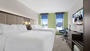 A hotel room with two beds, a desk, a chair, a TV, and a view of the city.