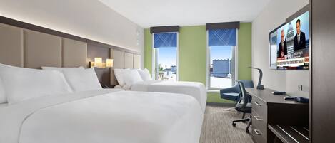 A hotel room with two beds, a desk, a chair, a TV, and a view of the city.