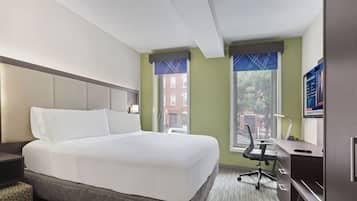 Camera d'albergo con un letto grande, una scrivania con sedia e una finestra vista edifici.