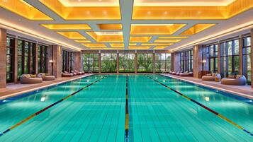 A large indoor swimming pool with clear lane dividers, large windows, and seating areas along the sides.
