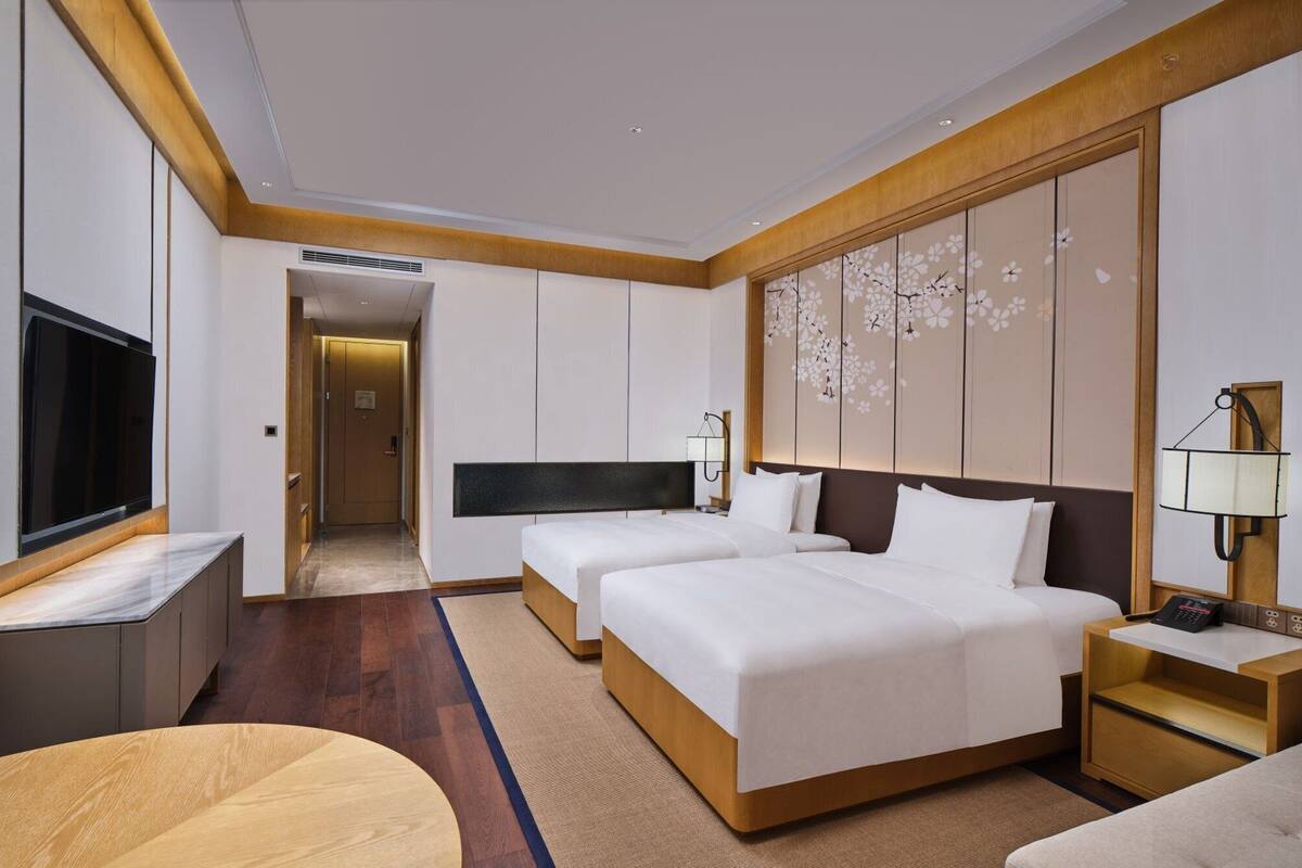 A hotel room with two beds, a TV, a desk, and a wooden floor.