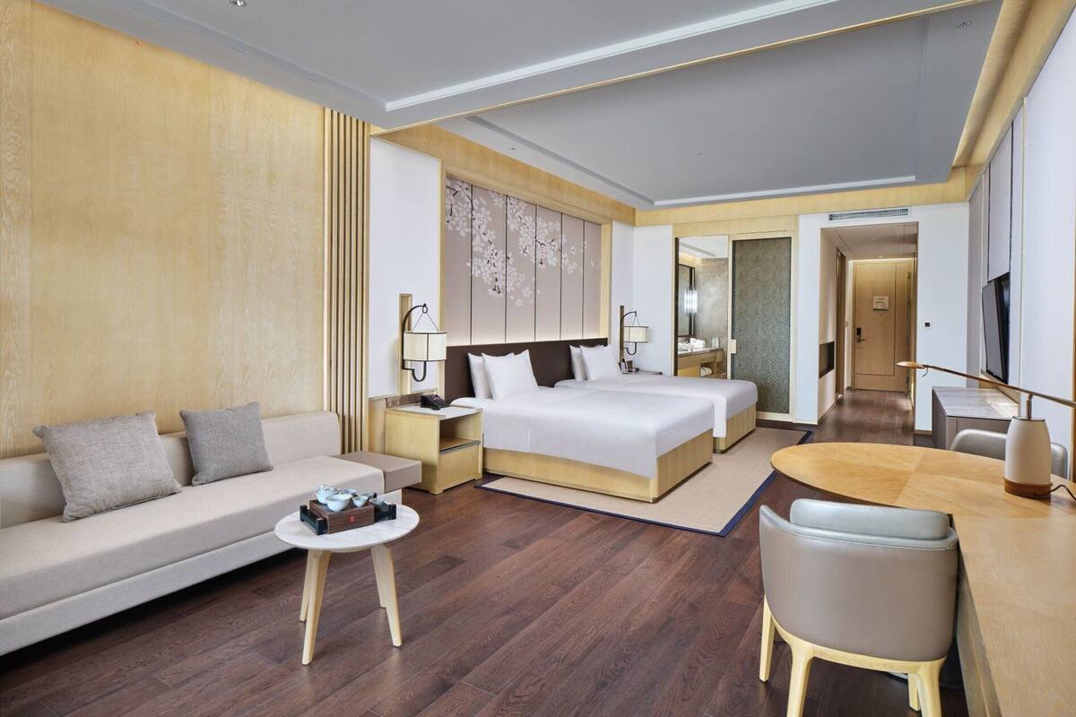 A modern hotel room with a large bed, a sofa, a dining table, and a TV.