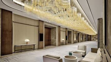 Un moderno vestíbulo de hotel con un largo pasillo, zonas de estar e un candelabro decorativo.