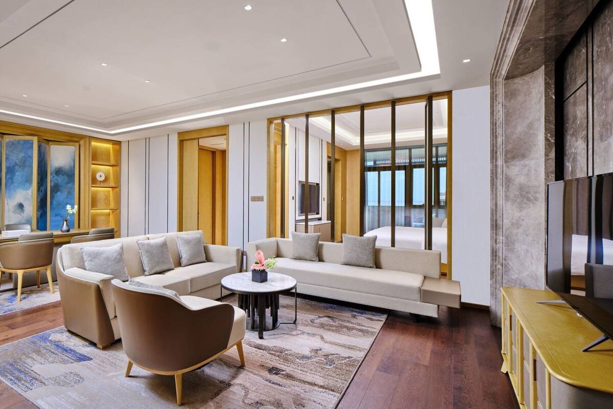 A modern hotel room with a sofa set, a coffee table, a TV, and a desk with a chair.