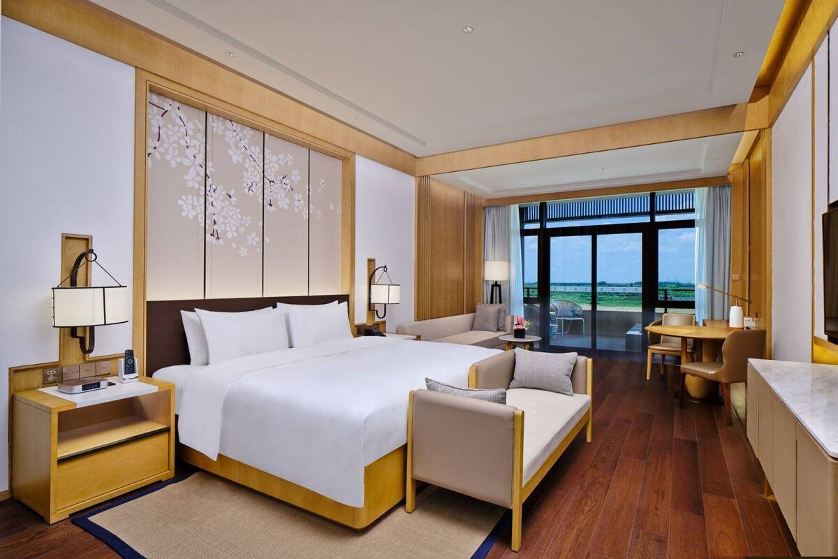 A hotel room with a large bed, a sofa, a desk, and a TV.