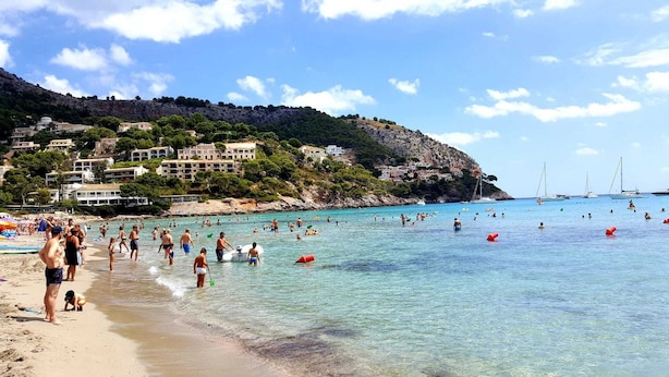 Une plage avec une eau claire, des gens qui se baignent et des bâtiments en arri ère-plan.