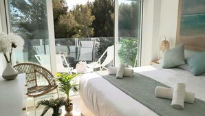 Une chambre moderne avec un grand lit, un coin salon comprenant une chaise et une table, et un balcon avec des chaises et une plante.