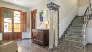 Una habitación amplia con suelo de madera, un aparador de estilo vintage, una puerta de madera grande y una escalera con columnas de mármol.