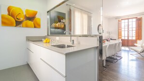 Una cocina moderna con una isla grande, un comedor con mesa y sillas, y un ventanal con cortinas.