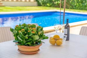 Una mesa con una planta en maceta, un cuenco de limones y una botella de vino, con vista a una piscina.