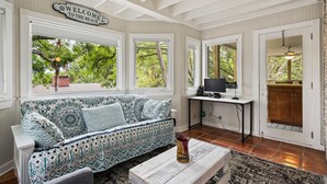 A room with a patterned sofa, a coffee table, and a desk with a computer. There are large windows with a view of greenery outside. - Steps from the beach with private pool Oceanview Home rooftop view 5BR Sleep 15 (St. Simons Island)