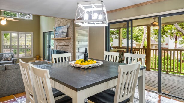 A dining area with a dark wooden table, white chairs, and a fruit bowl. There is a ceiling fan and a hanging light fixture. - Steps from the beach with private pool Oceanview Home rooftop view 5BR Sleep 15 (St. Simons Island)