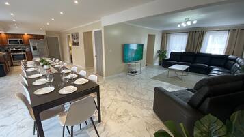 A modern living room with a black leather sofa, a dining area with a marble floor, and a kitchen with stainless steel appliances.