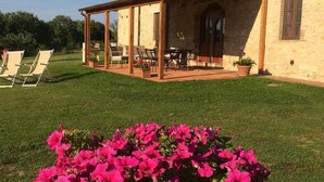 Una casa con un patio cubierto, césped y una cama de flores con flores rosadas.