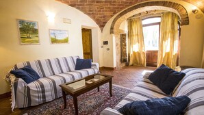 Una sala de estar acogedora con un sofá a rayas, una mesa de centro y un tapete estampado. Hay dos cuadros en la pared, una puerta de madera y una ventana con cortinas.