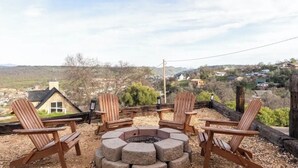 A fire pit surrounded by four wooden Adirondack chairs, overlooking a scenic landscape with houses and hills. - Explore natures retreat with amazing views of Lake Tulloch and close to Yosemite (Copperopolis)